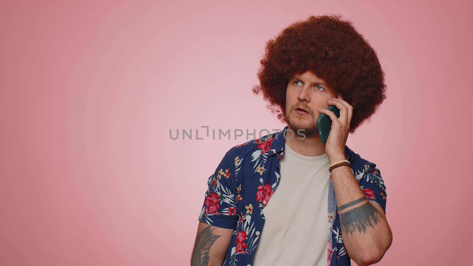 Tired sleepy freelancer tourist man talking on mobile phone with friend, making online conversation. Disinterested young guy boy having annoyed boring talk on smartphone isolated on blue background