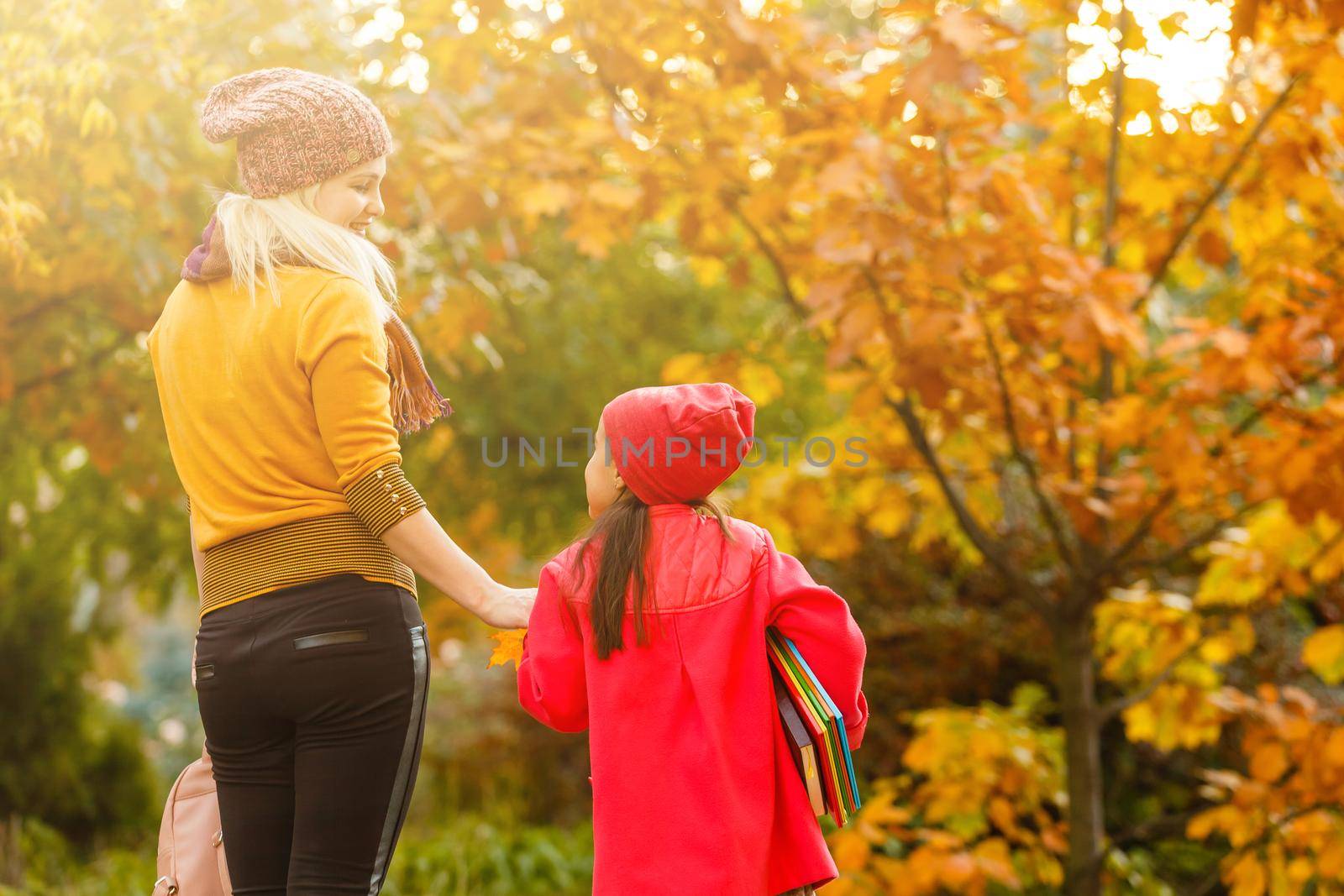 Mom leads her daughter to school. Return to school. Woman and girl with backpack behind the back. Beginning of lessons. First day of fall.