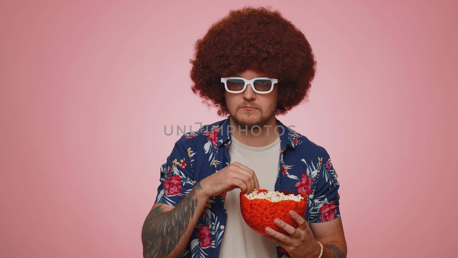 Excited tourist man in 3D glasses enjoying eating popcorn and watching interesting tv serial sport game, film, online social media movie content. Young guy boy isolated alone on blue studio background