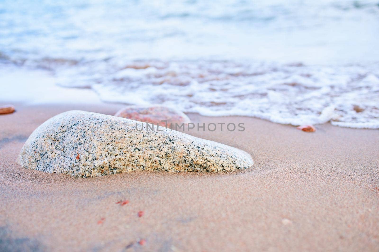 Sandy beach with waves from the sea. Rock in sand near the ocean.