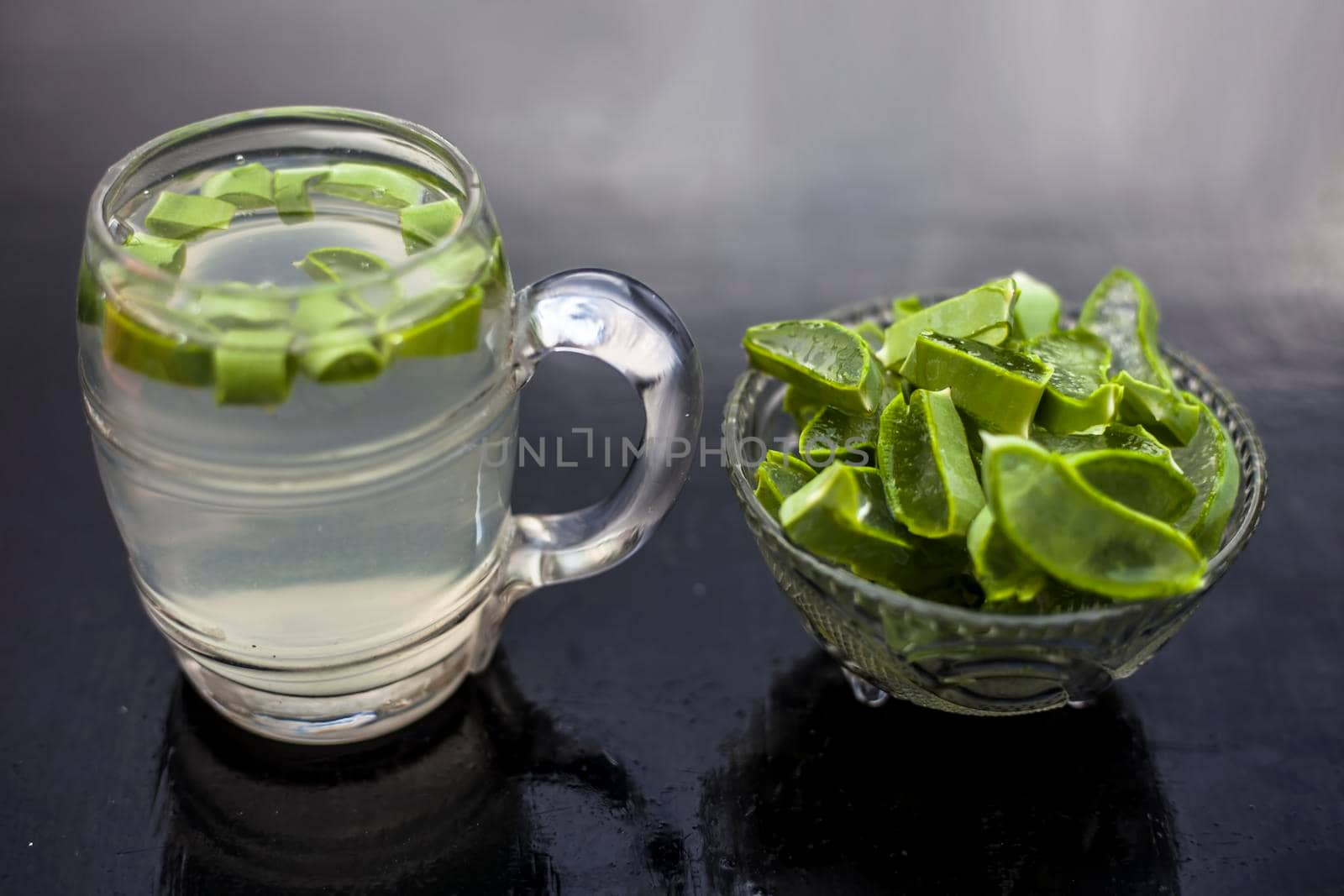 Close up of glass mug on wooden surface containing aloe vera detox drink in along with its entire raw ingredients with it. Horizontal shot with blurred background. by mirzamlk