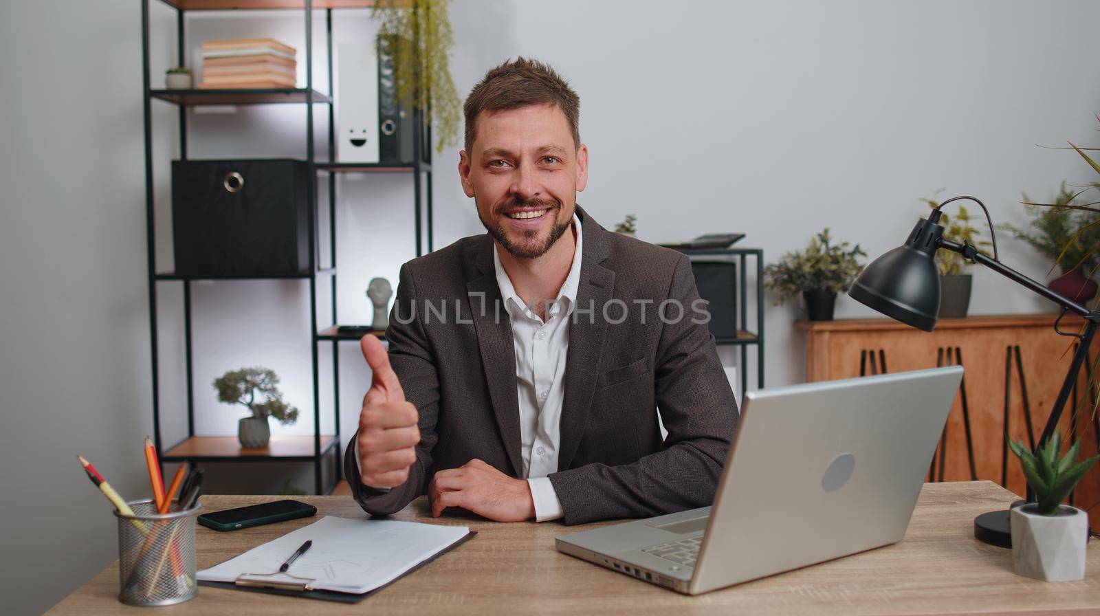 Like. Happy businessman in suit working on laptop looking approvingly at camera showing thumbs up, like sign positive something good, positive feedback at office workplace desk. Freelancer adult man