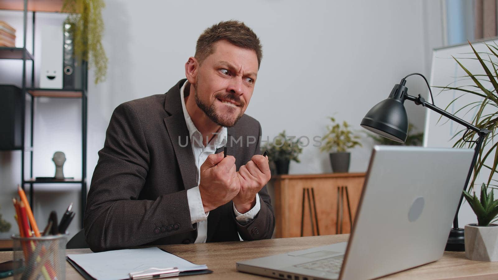 Businessman working on laptop analyzing financial graph decrease loses becoming surprised sudden results, bad news, fortune loss fail at office. Irritated angry freelancer man breaking pencil in hands