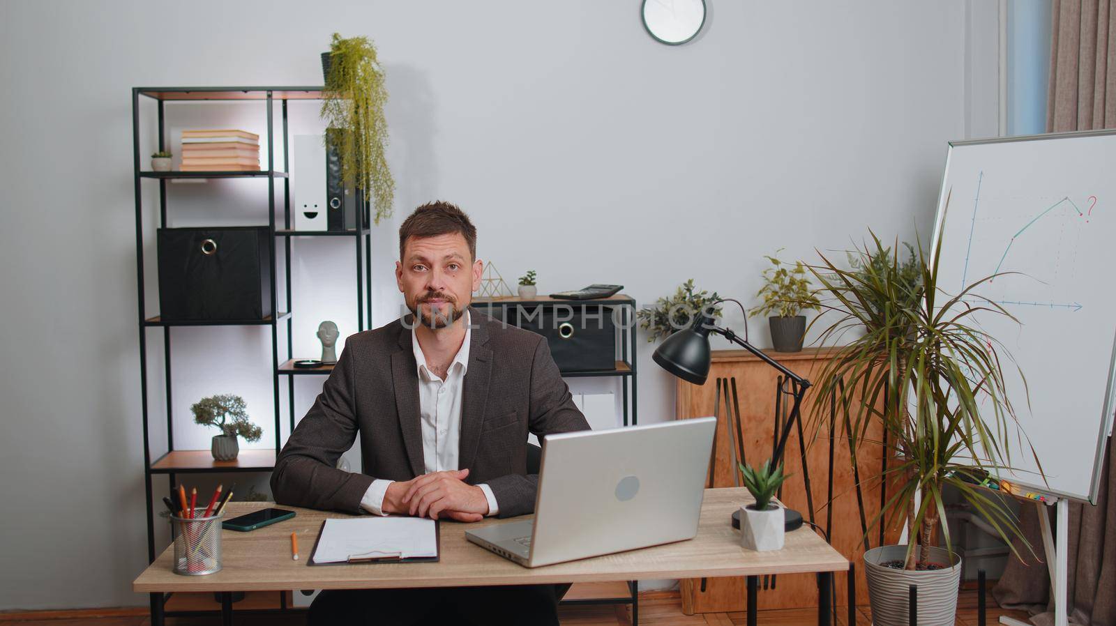 Businessman in suit thinking about an important creative project work decision at home office desk. Confident serious male manager freelancer man busy occupation looking through analytical reports