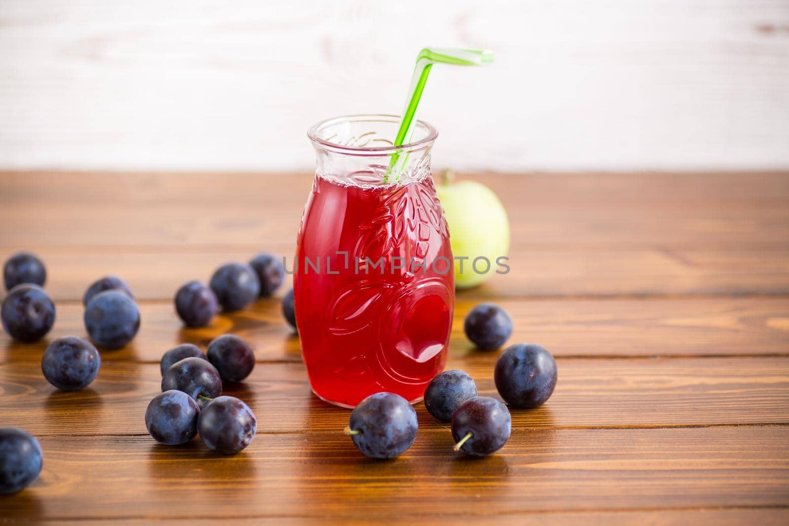 Sweet natural plum drink in a glass with a straw on a wooden table