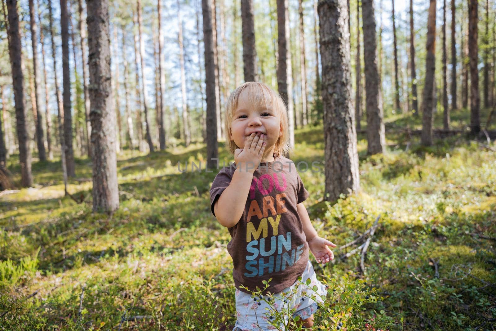 Blond Baby girl picking and eating berries in the forest by Varaksina