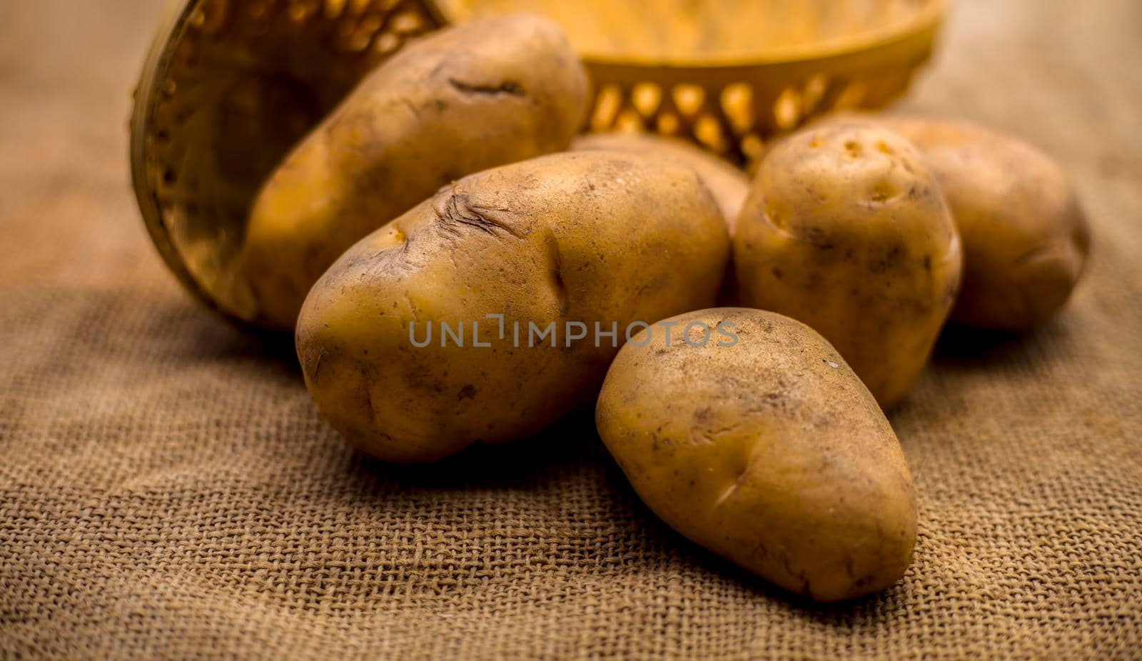 Close up shot of potato or aloo or alu on jute bag surface along with two vegetable and fruit hampers.