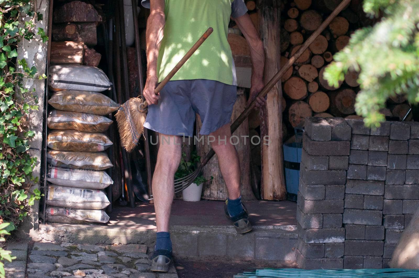 gardener in dirty work clothes and boots holds garden tools, plastic brush broom, seasonal spring work in the garden. High quality photo