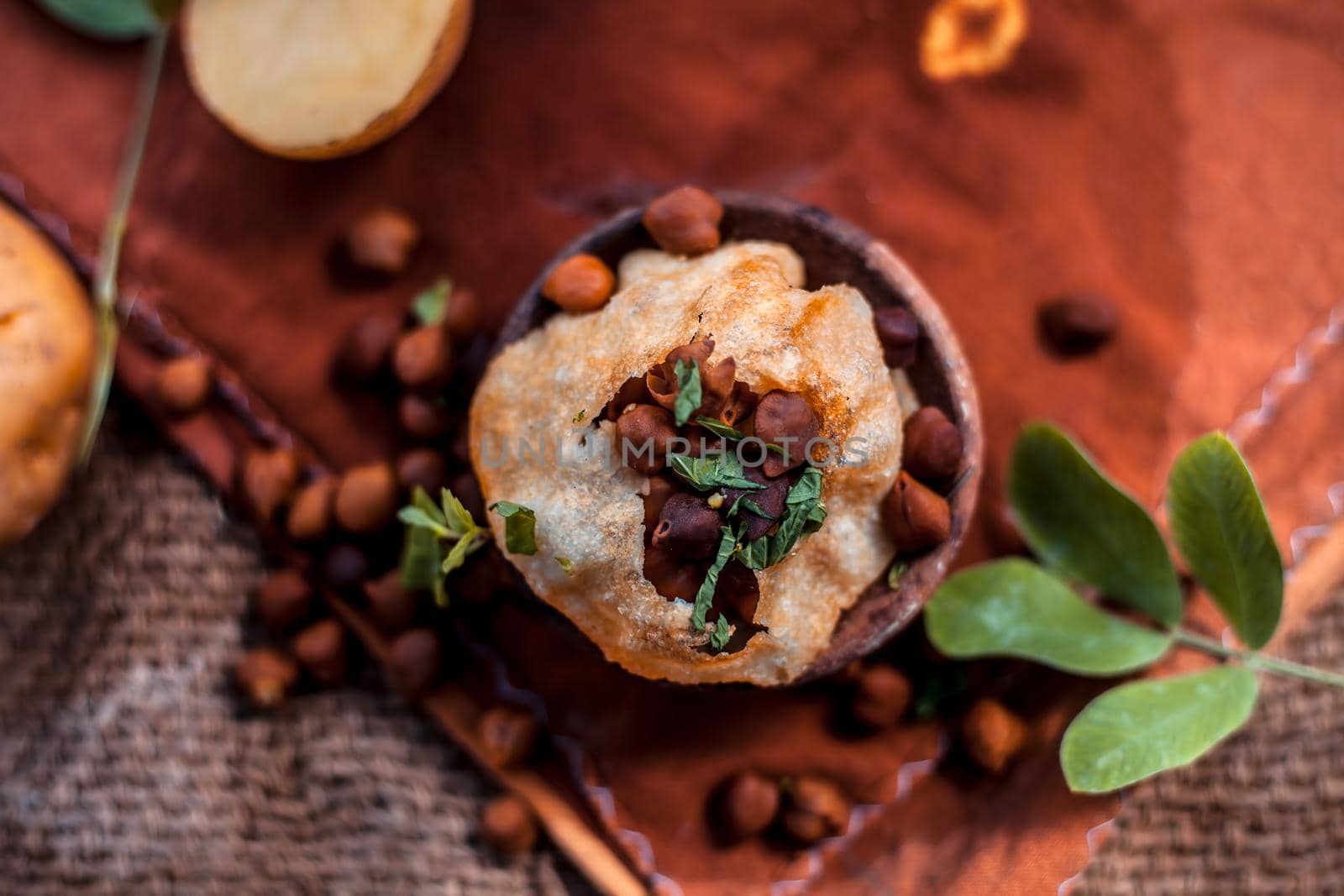 Famous Indian & Asian street food dish i.e. Panipuri snack in a clay bowl along with its flavored spicy water in another clay vessel. Entire consisting raw ingredients present on the surface.Top shot.