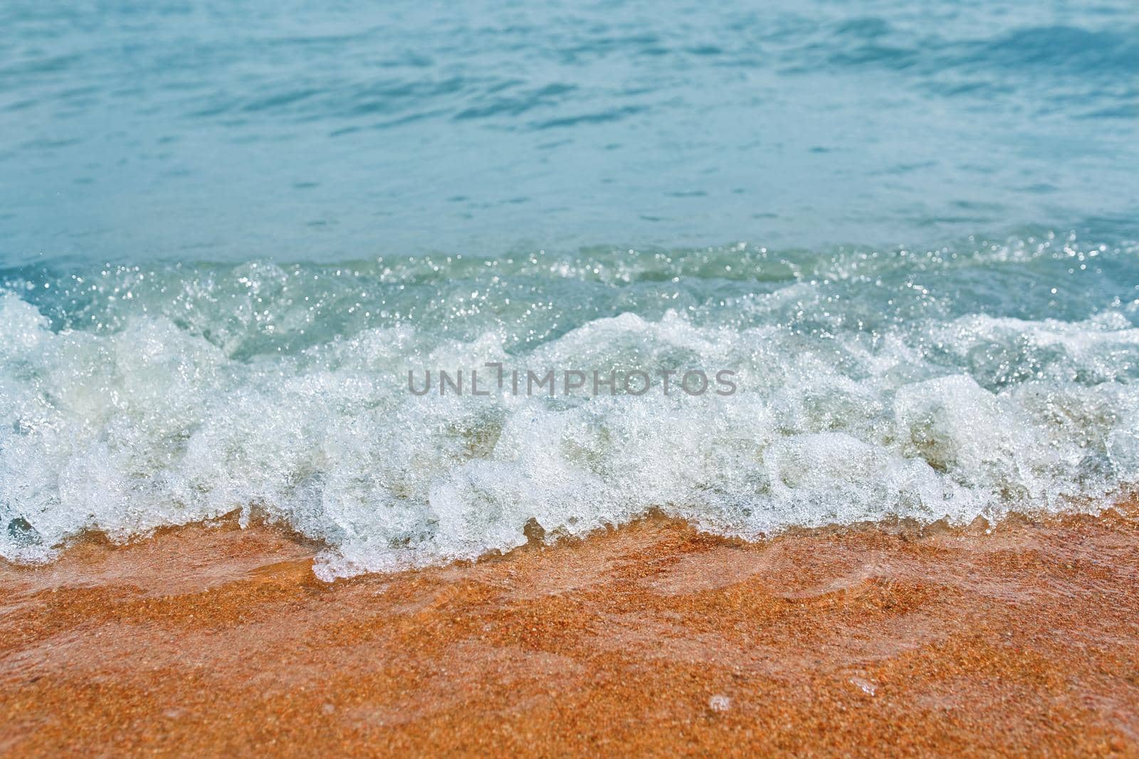 Sandy beach with waves from the sea. Ocean water close up.