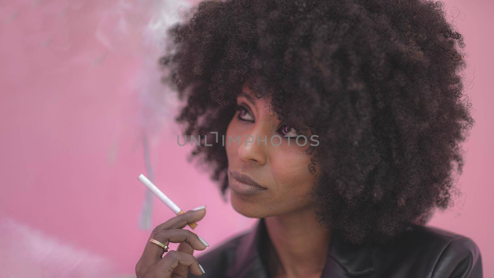 Young attractive African woman with happy cheerful smile smoking in studio