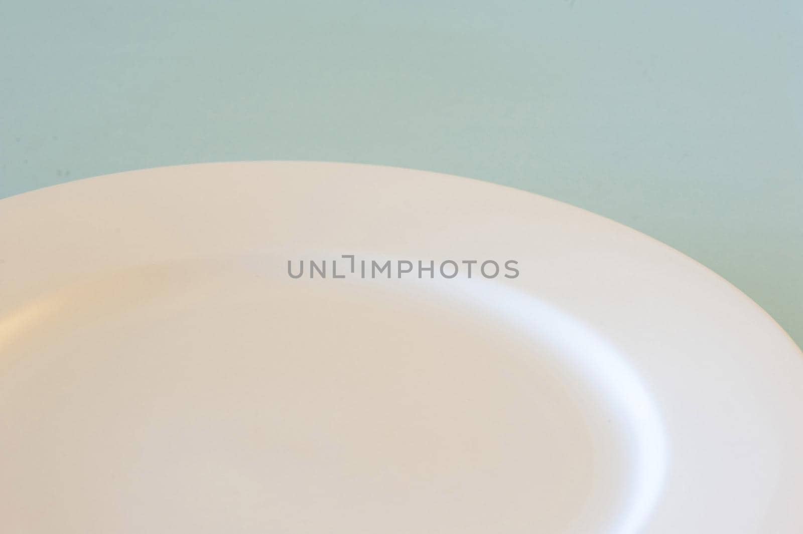 Partial view of an empty clean white dinner plate over a blue background for food placement