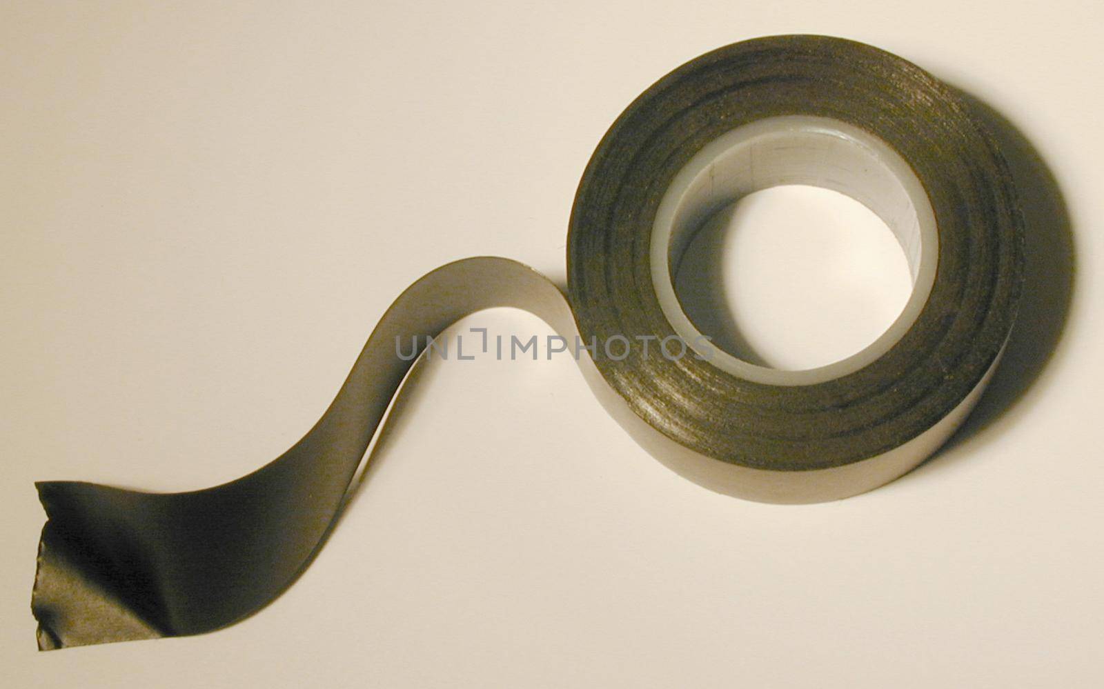 Roll of black plastic insulation tape from above with one end unrolled over a white background with copy space