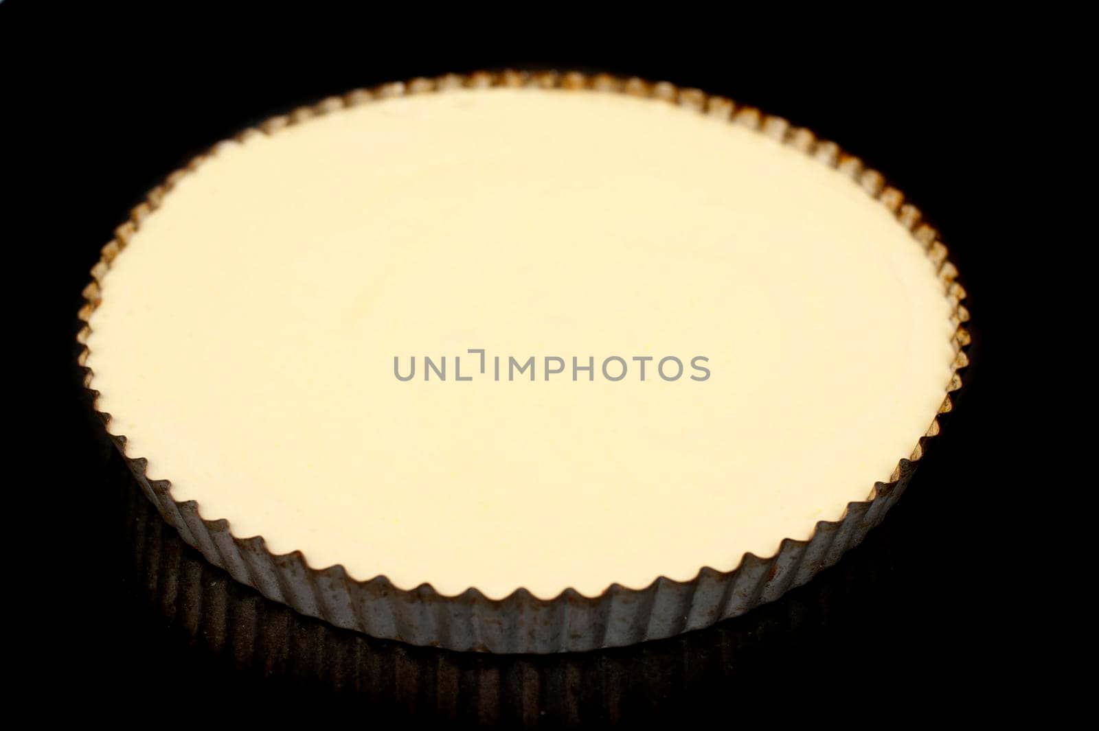 High angle view of a delicious plain baked cheesecake in a round fluted metal oven dish or pie pan on a dark studio background