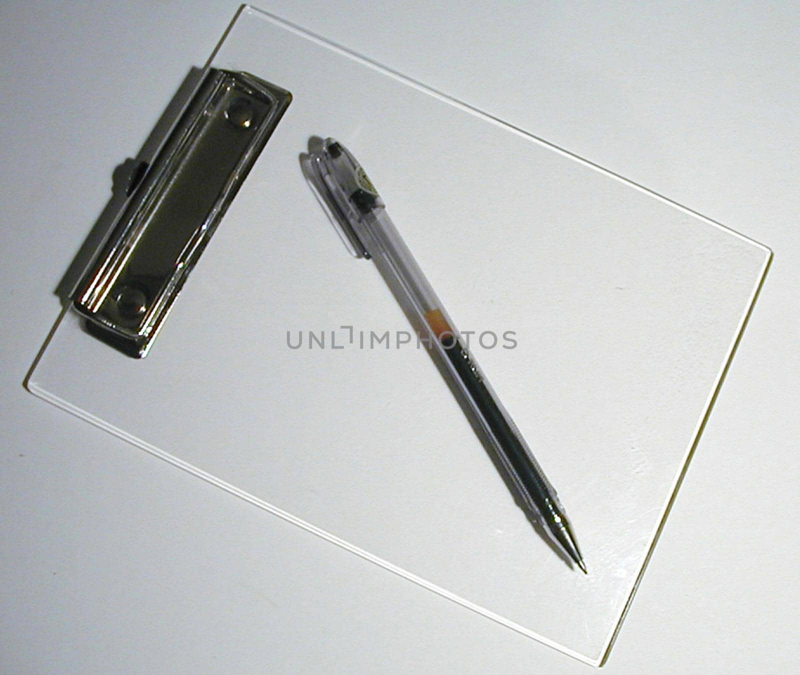Empty white clipboard with pen lying diagonally on a white background viewed from overhead