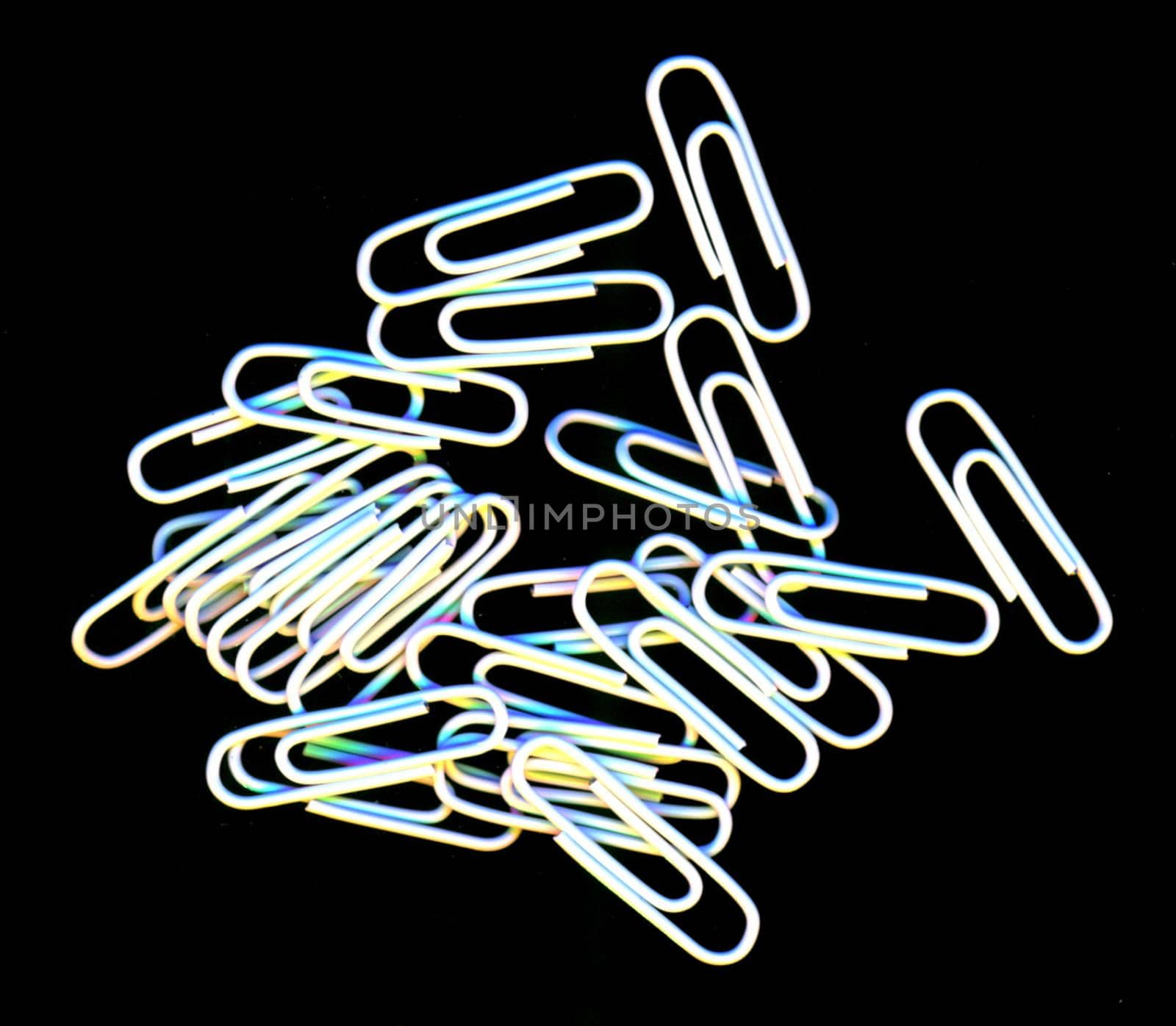 Scattered pile of white paperclips for filing documents and making attachments lying on a black background, overhead, view