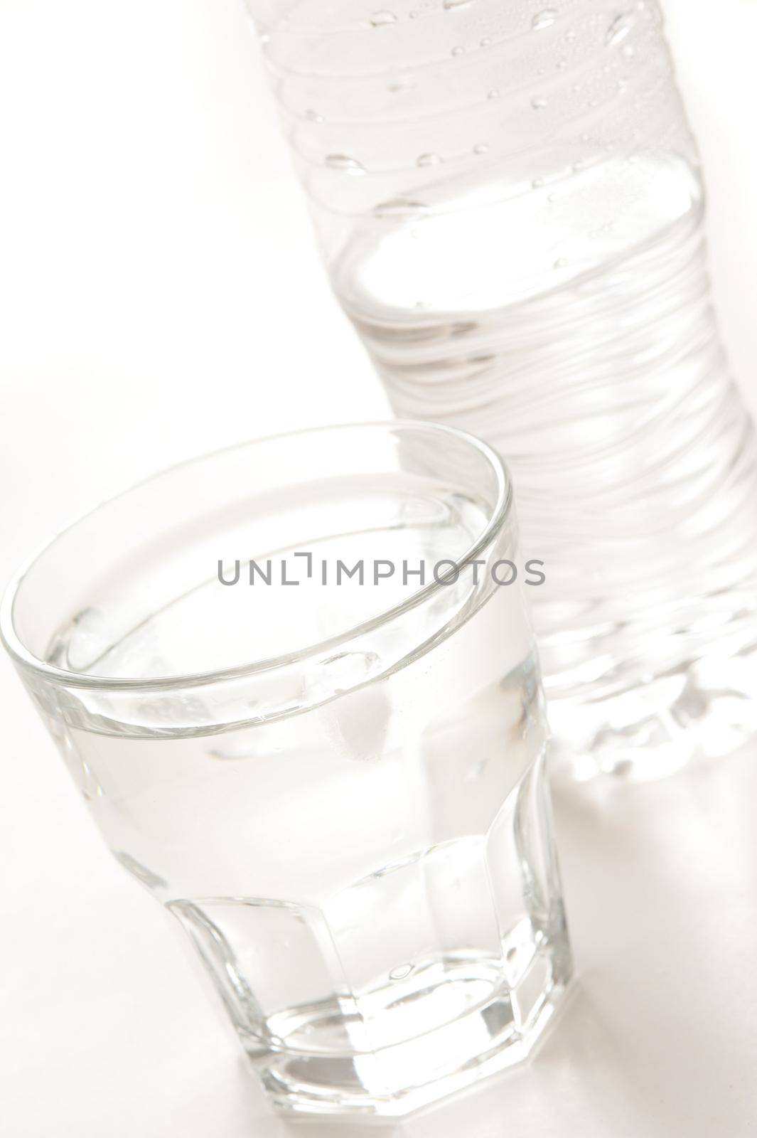 Glass of clear clean pure bottled water with the plastic bottle behind on a white background, close up tilted angle