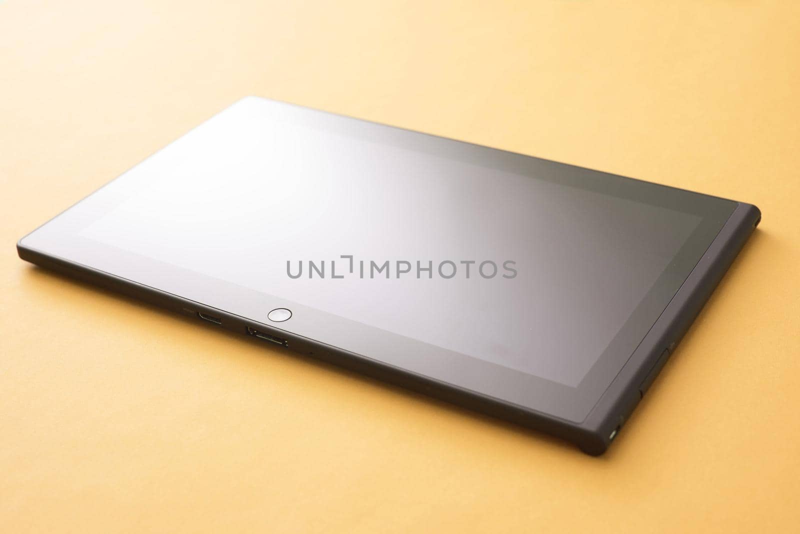 Tablet mobile device with blank black screen close-up on yellow surface with studio lighting