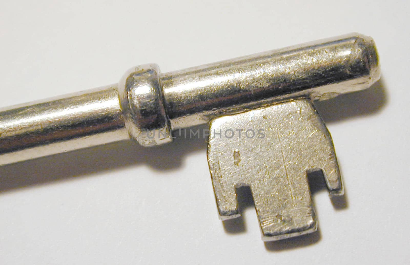 Metallic lever lock key with collar and symmetrical wards, close-up with shadow and copy space on gray