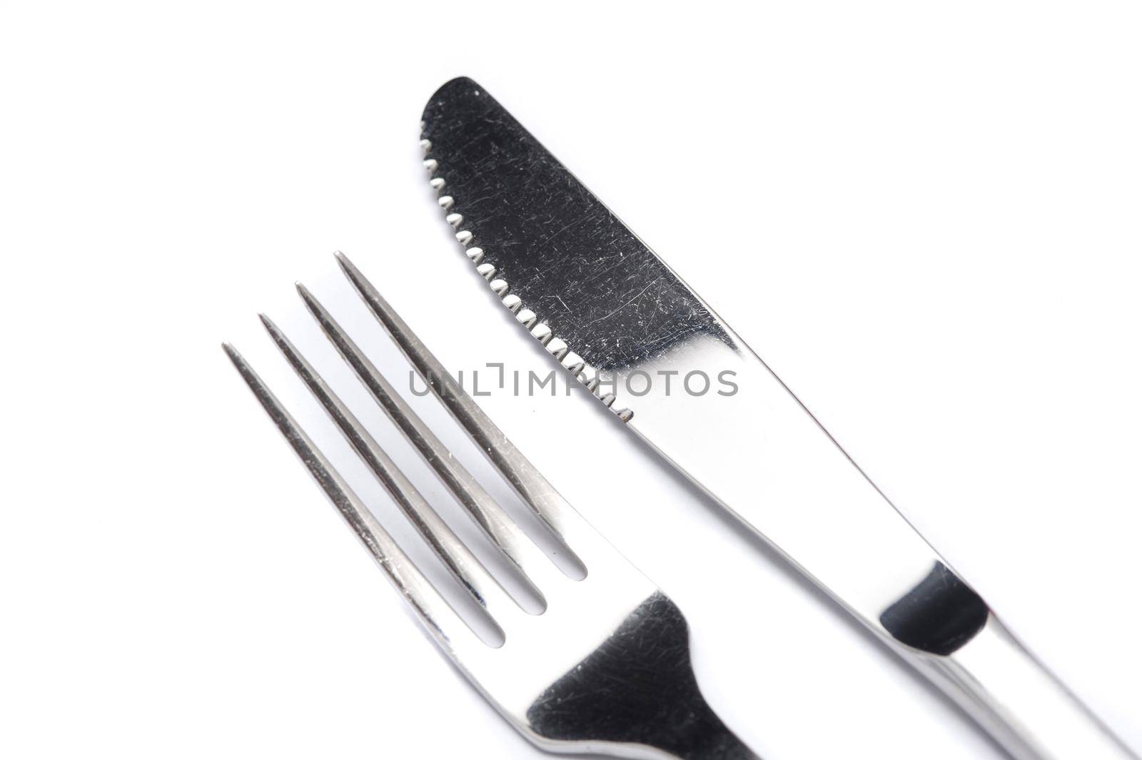 Clean silver knife and fork close up on white arranged diagonally from the corner viewed from above in a catering concept