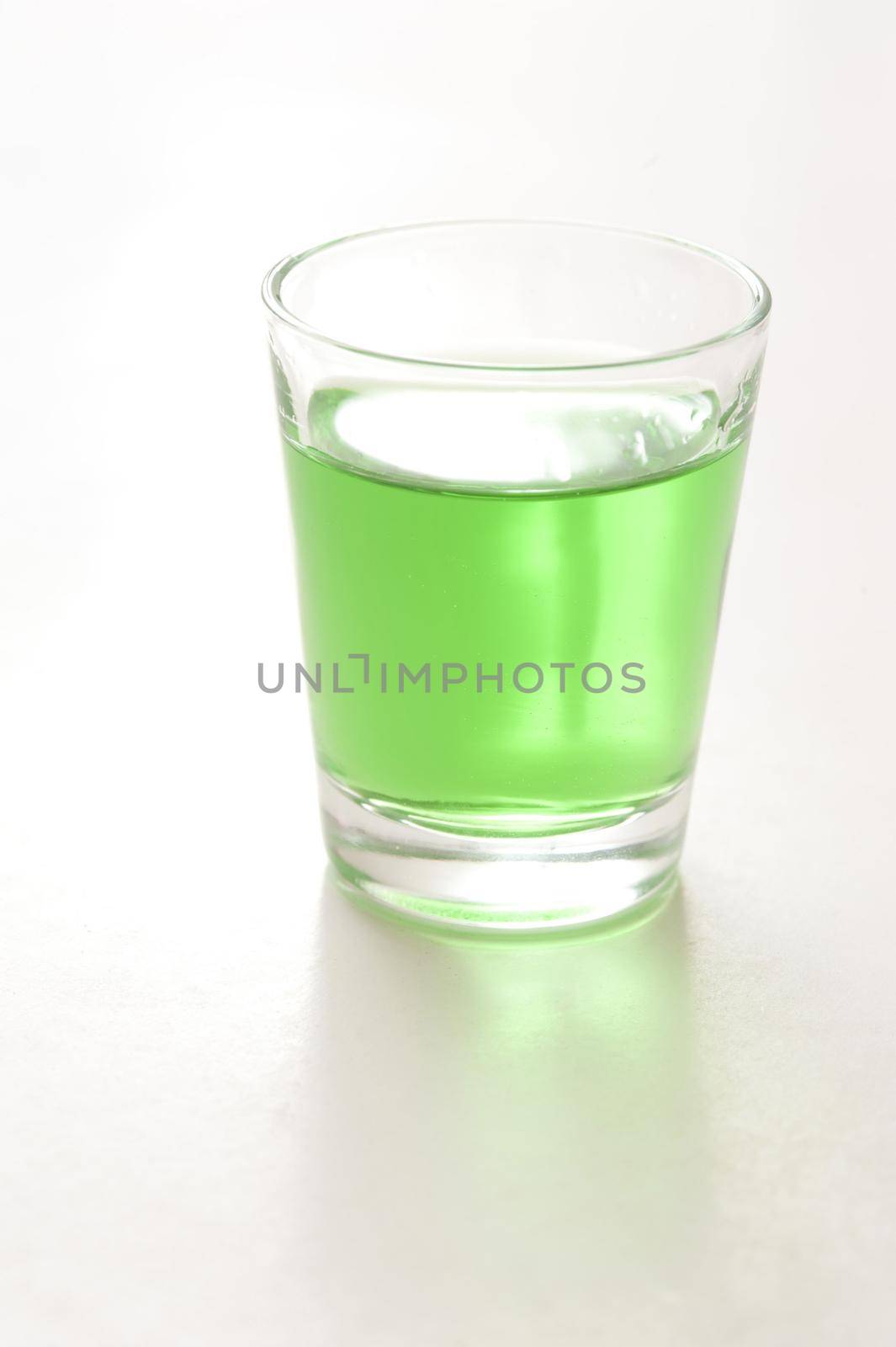 Shot glass of green absinthe, a potent alcoholic spirit with a taste of anise, on a reflective white background with copyspace