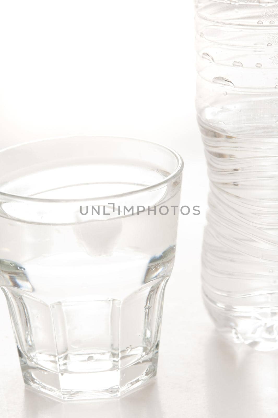 Glass of clean fresh bottled water with the unlabeled plastic water bottle standing alongside on white