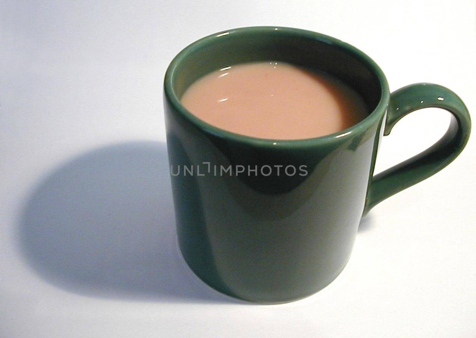 Close-up of a green porcelain mug full of hot coffee with milk, with shadow, on grey