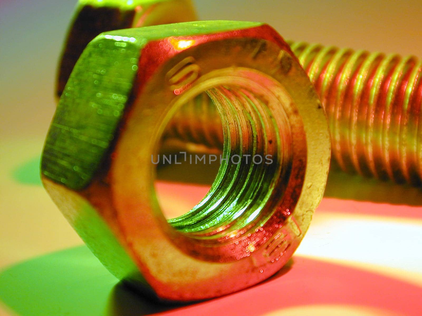 Nut and bolt in macro close-up, lit up with green and red colors. Engineering background concept