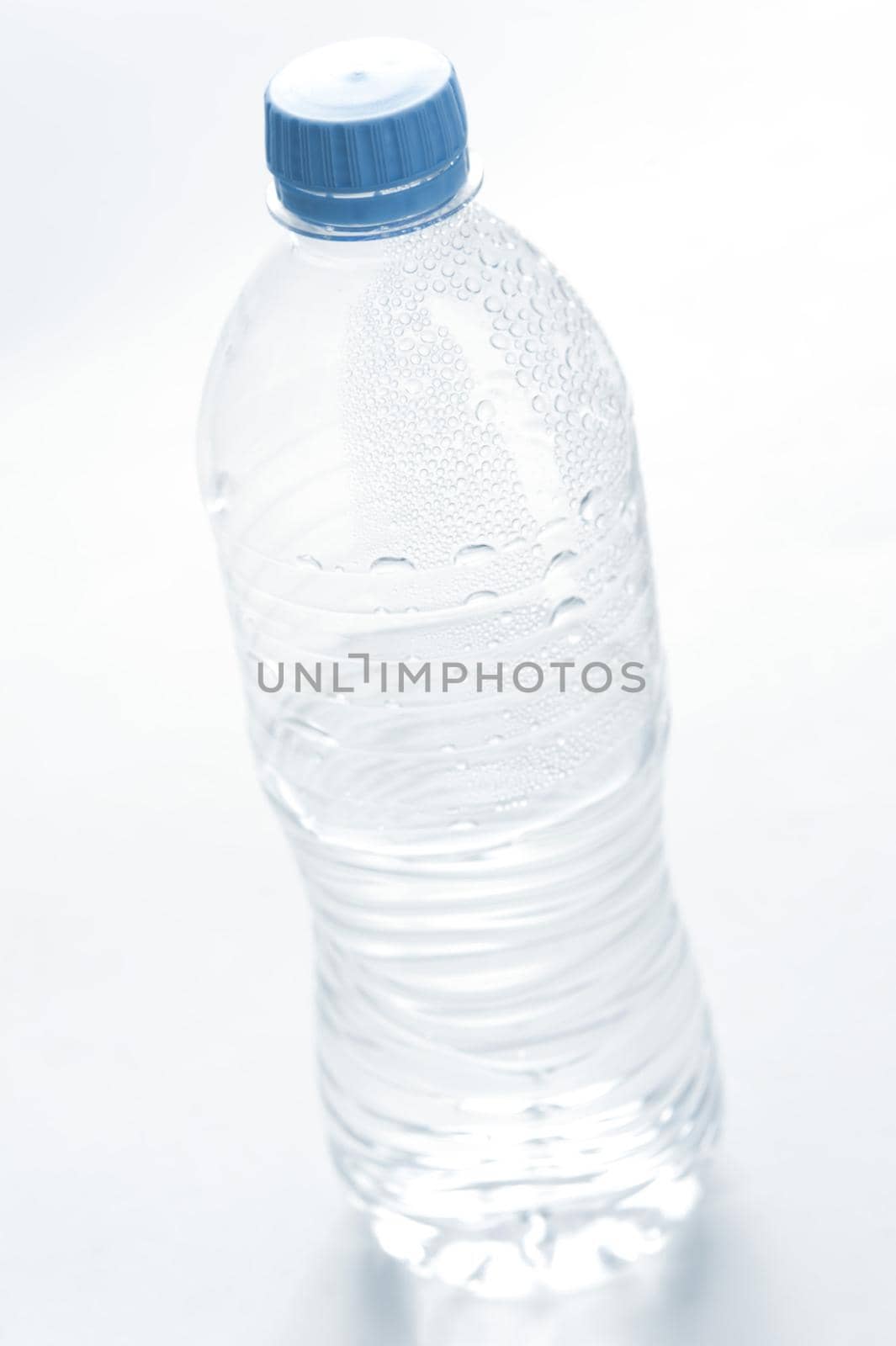 Plastic bottle of cold fresh pure mineral water with beaded condensation on the surface and a blue cap, unlabeled on white