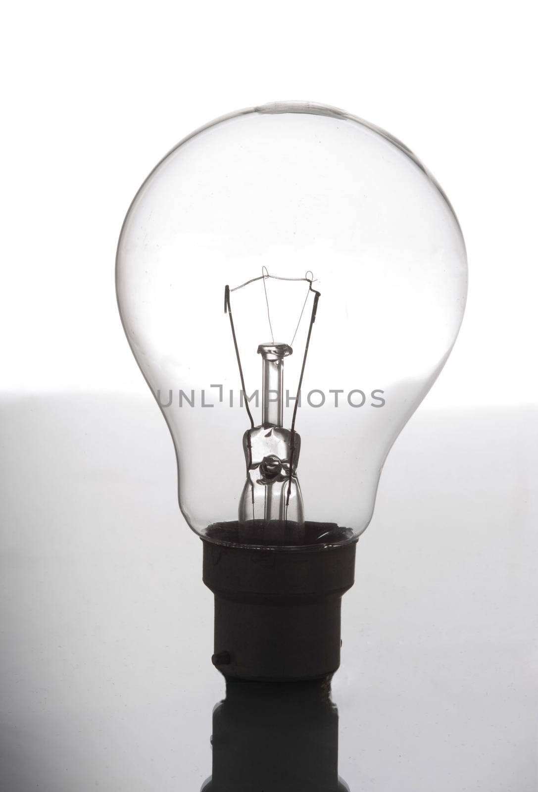 Transparent glass incandescent light bulb balanced upright on a reflective surface in a power and energy concept