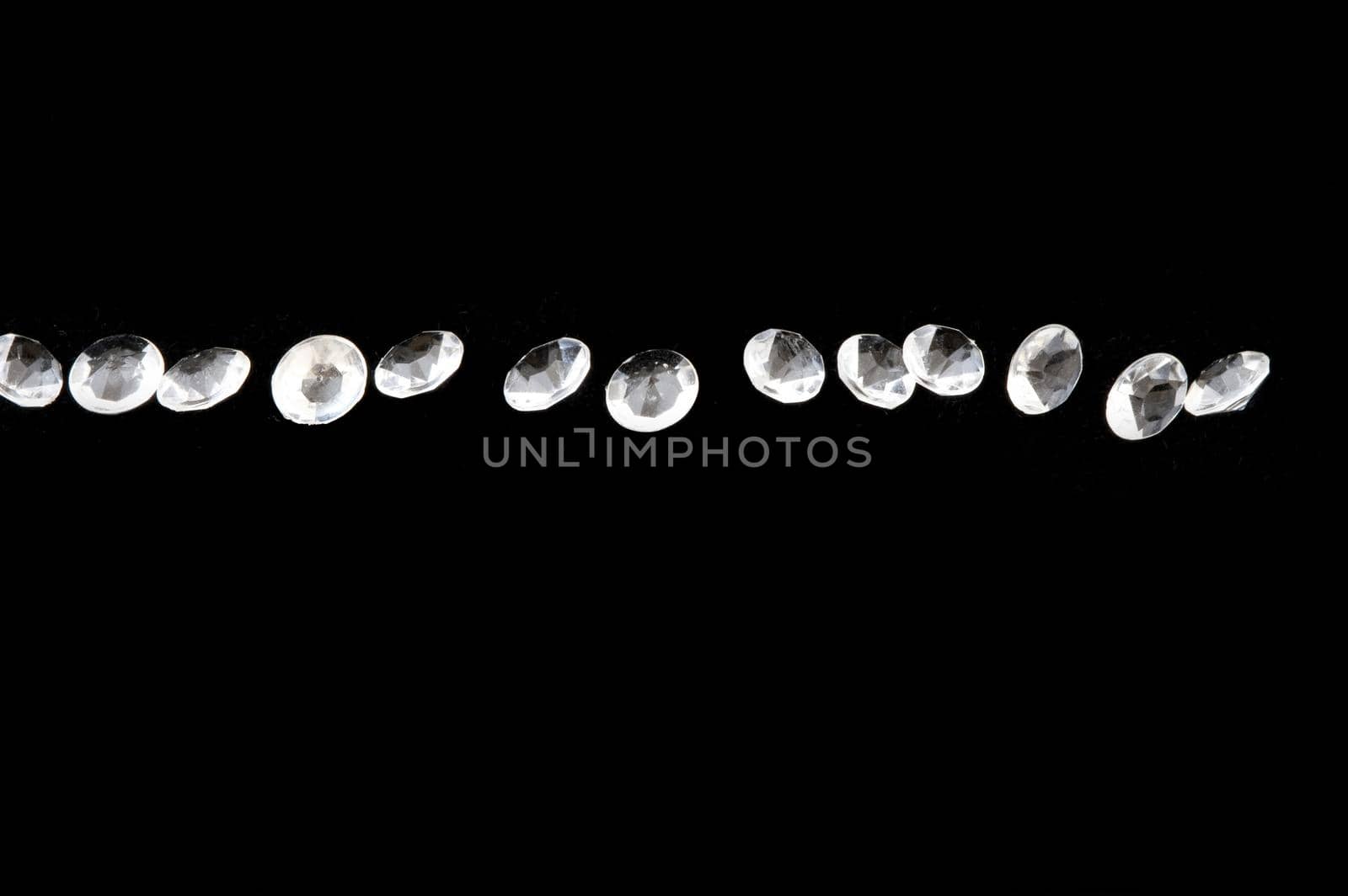 Line of bright diamond like stones over black with copy space above and below them