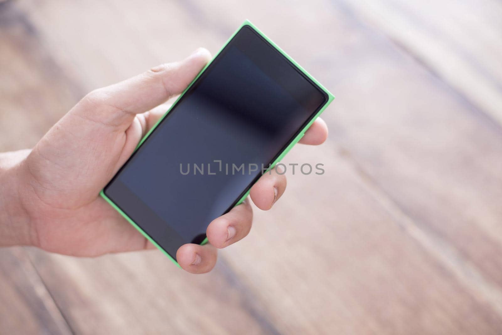 Close up of a man holding a smart phone in his hand with a blank, black screen against a plain background.