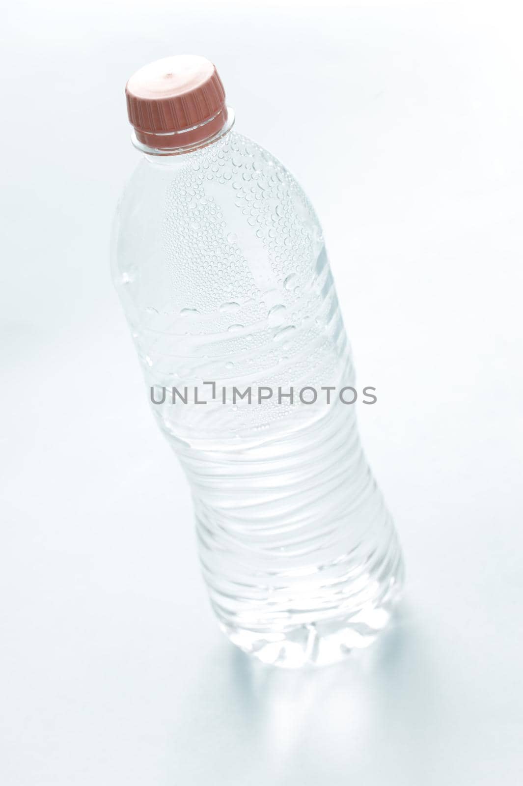Pure water in an unlabeled closed plastic bottle, tilted high angle view on white