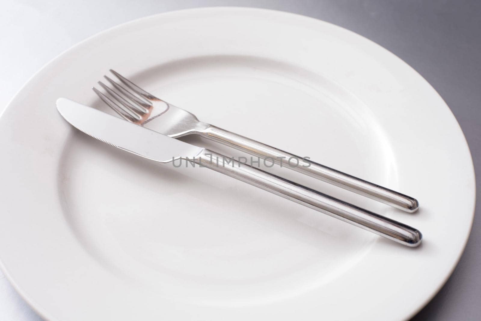 Plain generic silver metal knife and fork on a clean empty white dinner plate in a close up view