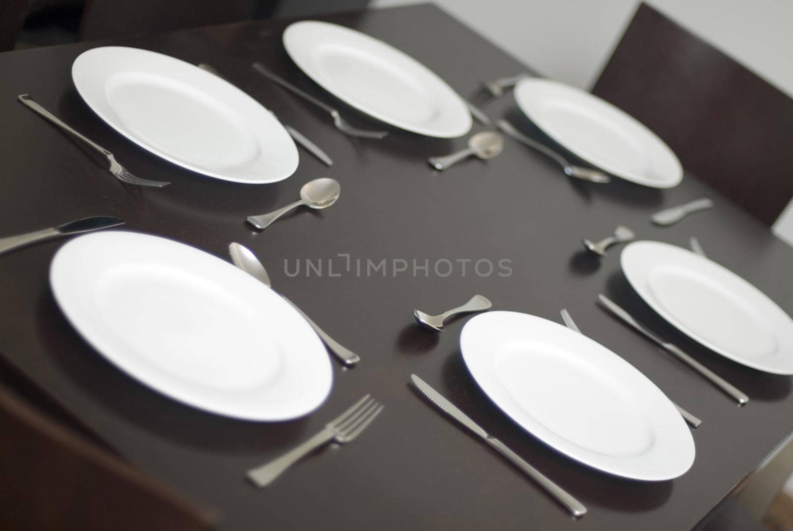 Place setting and generic white dinner plates with cutlery on a table with no food in a close up tilted angle view