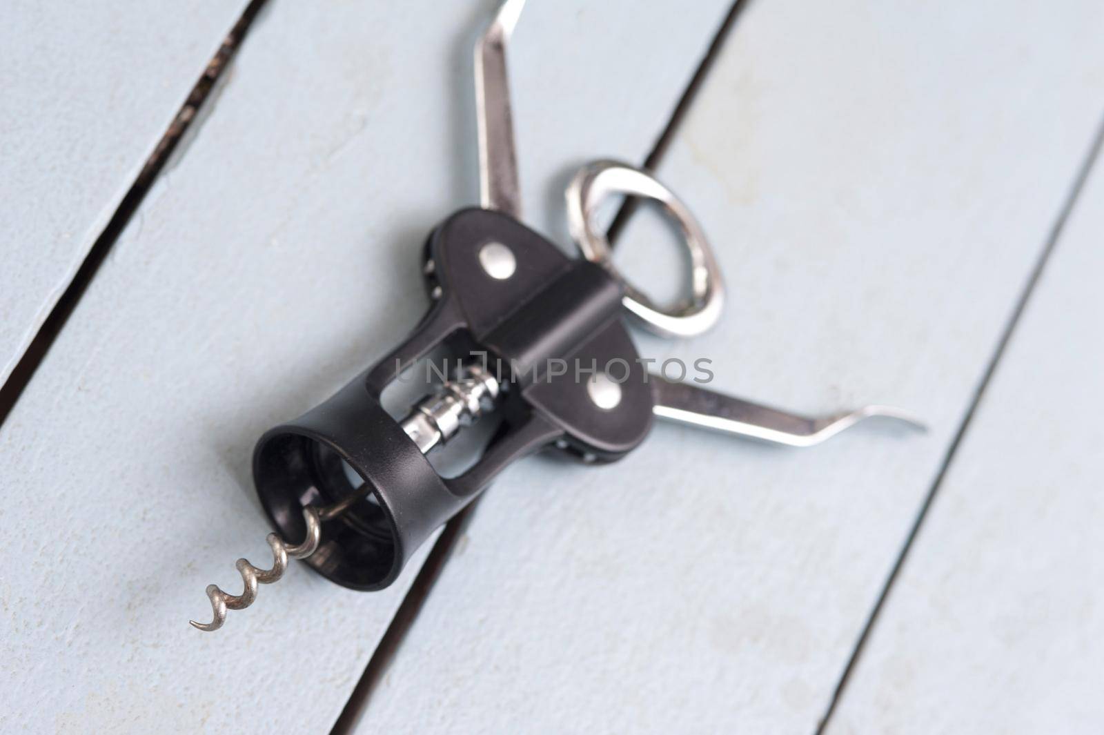 Lever style bottle opener for wine on a slatted white wooden table with the corkscrew in the foreground