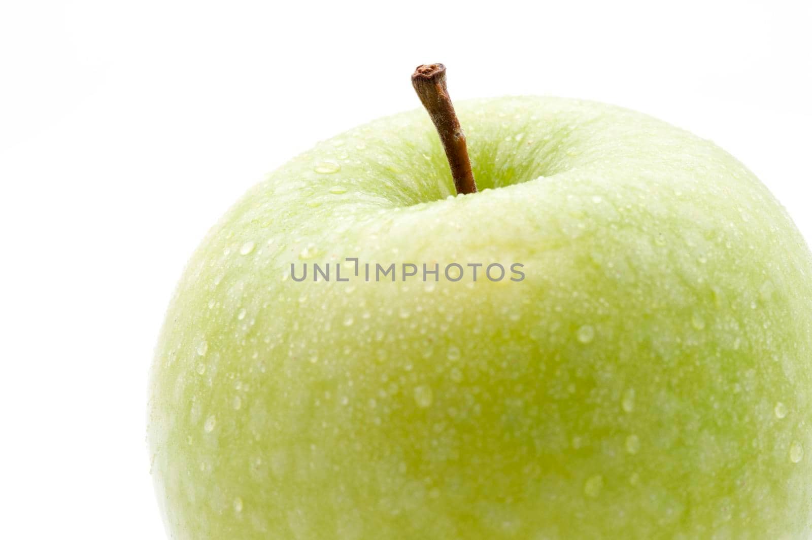 Closeup of a crisp healthy fresh green apple with water droplets and a stalk isolated on white