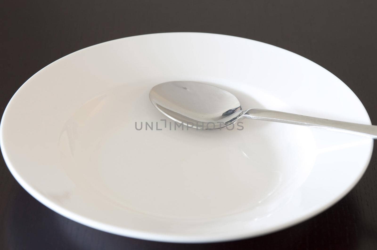 Empty clean white bowl and silver metal spoon in a close up view over black