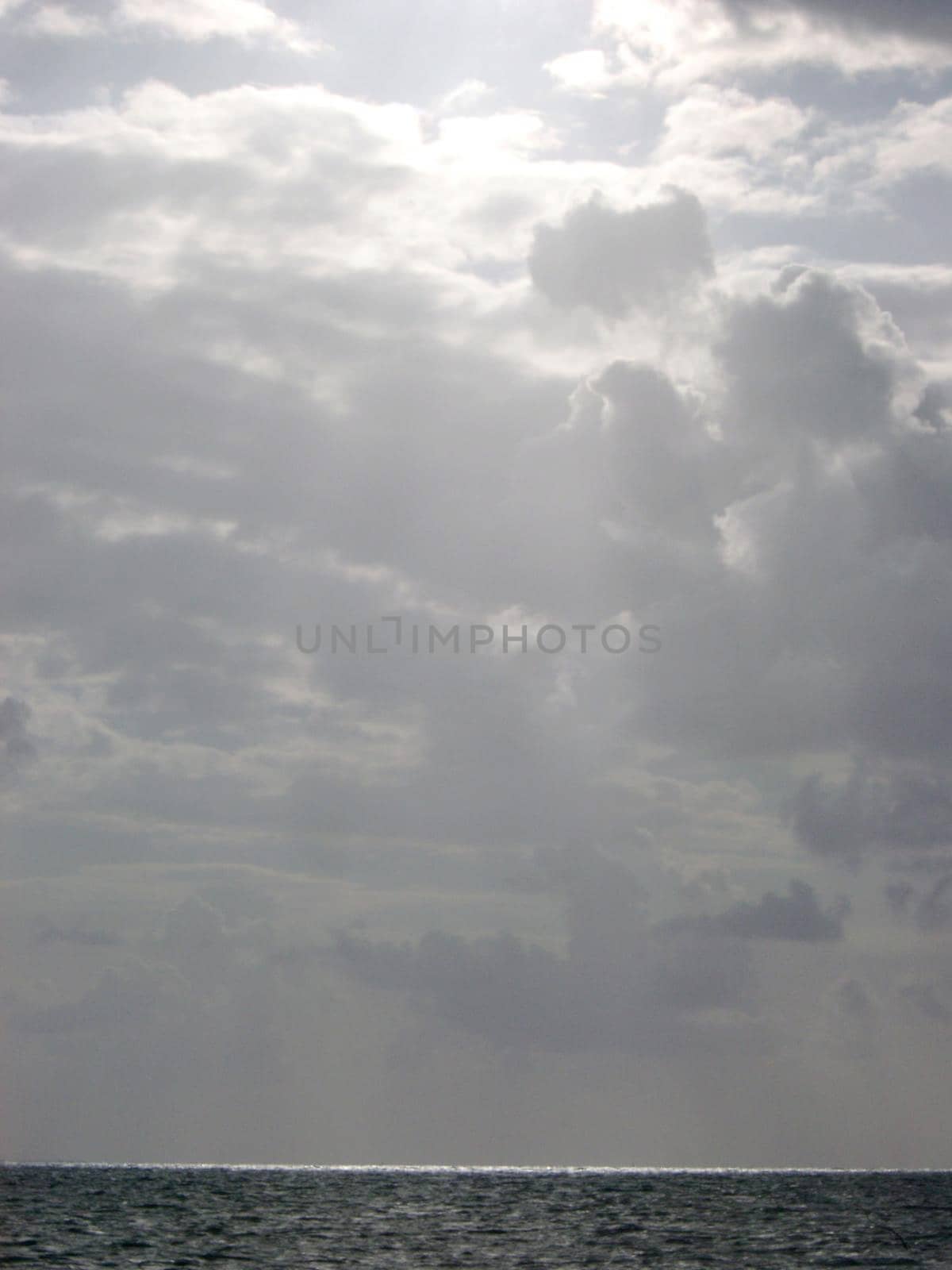 sun casting a beam of light onto the water from a storm sky