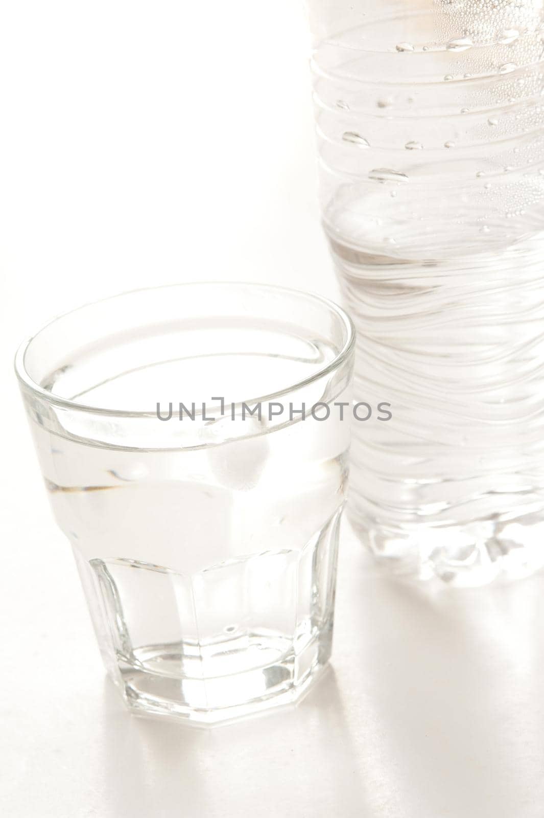 Glass of bottled water with a half full plastic bottle alongside on a white background with copyspace