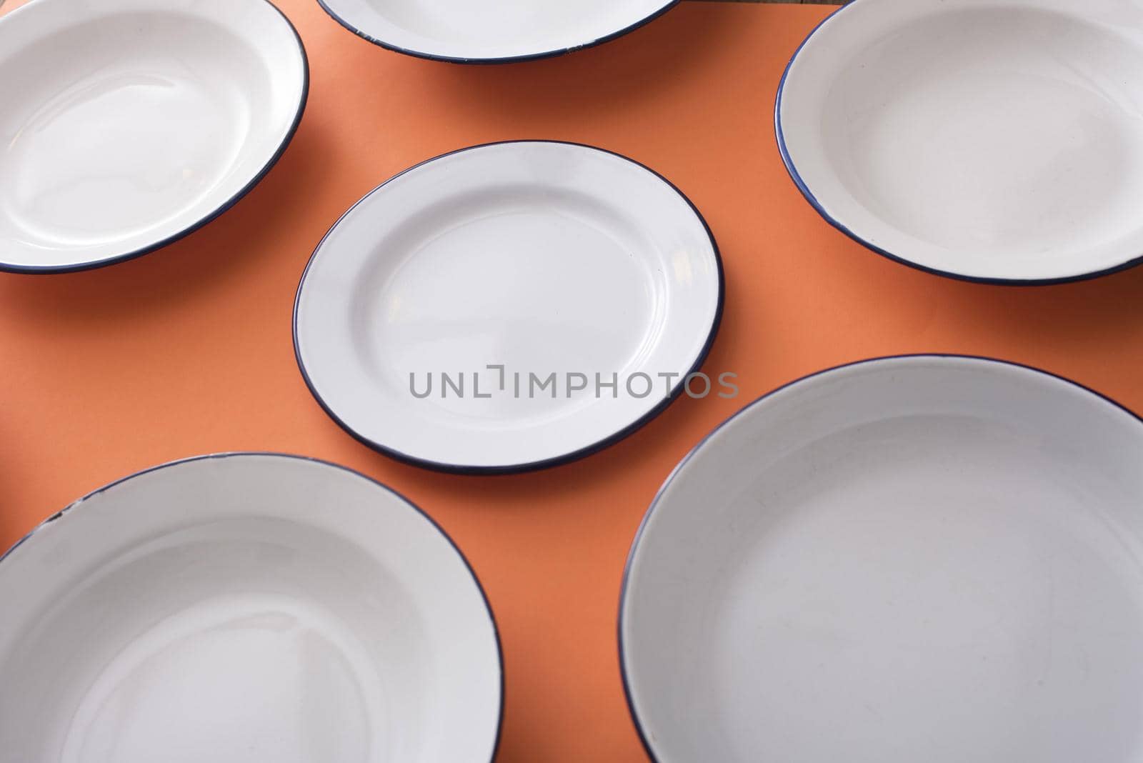 Plain white clean empty enamel plates on an orange background in a close up view and focus to a centre plate