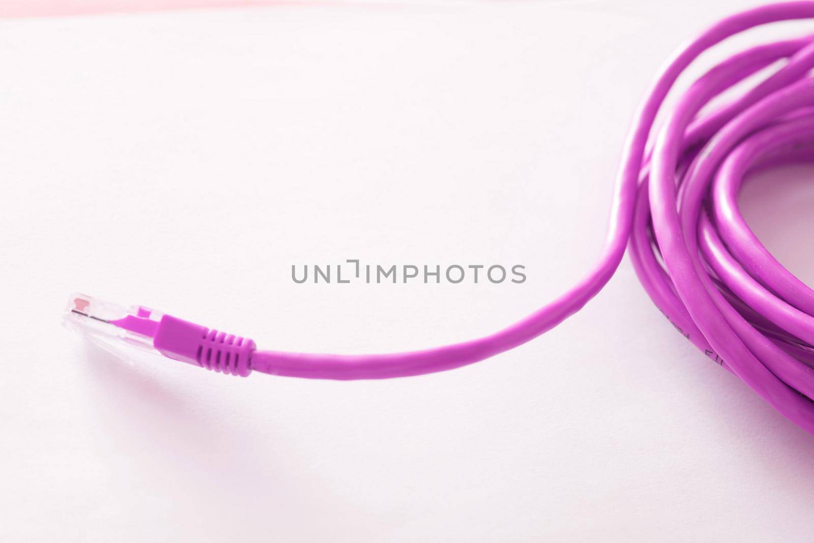 Bright vivid pink computer network cable and plug coiled on a white background with copy space in a communications concept