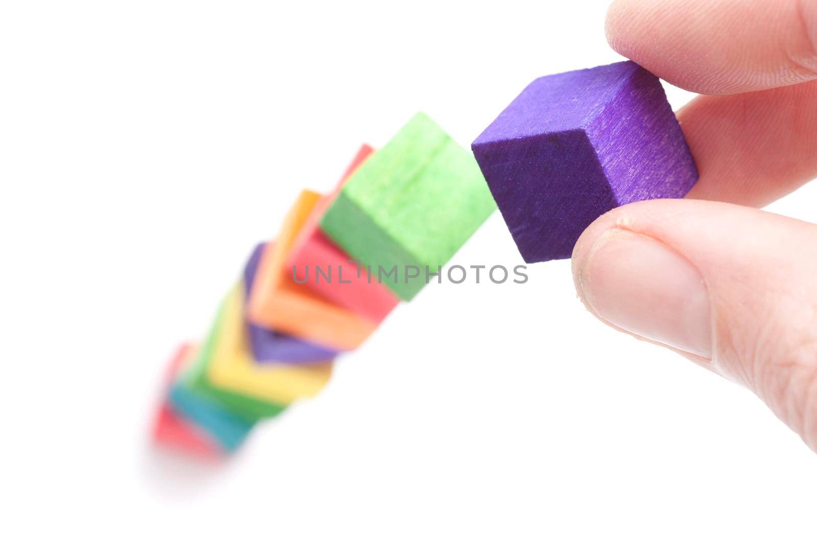 Cropped view image of a man building a tall tower with colourful toy wooden blocks with selective focus to the fingers and top purple block