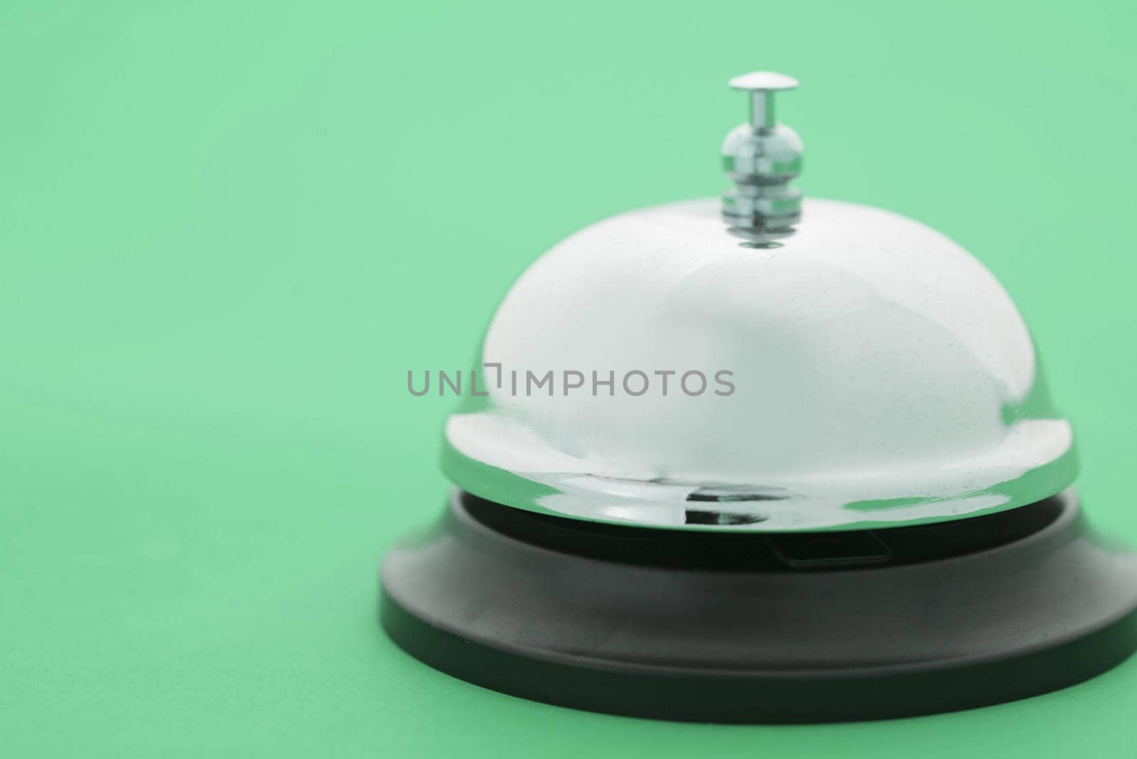 Close up of a shiny, silver service bell isolated on a plain green background.