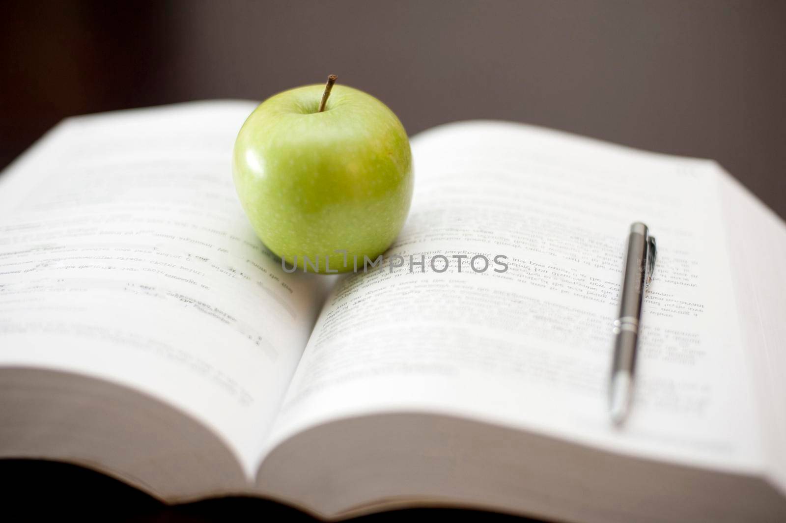 A fresh juicy green apple stands on an open textbook with a pen conceptual of education and learning