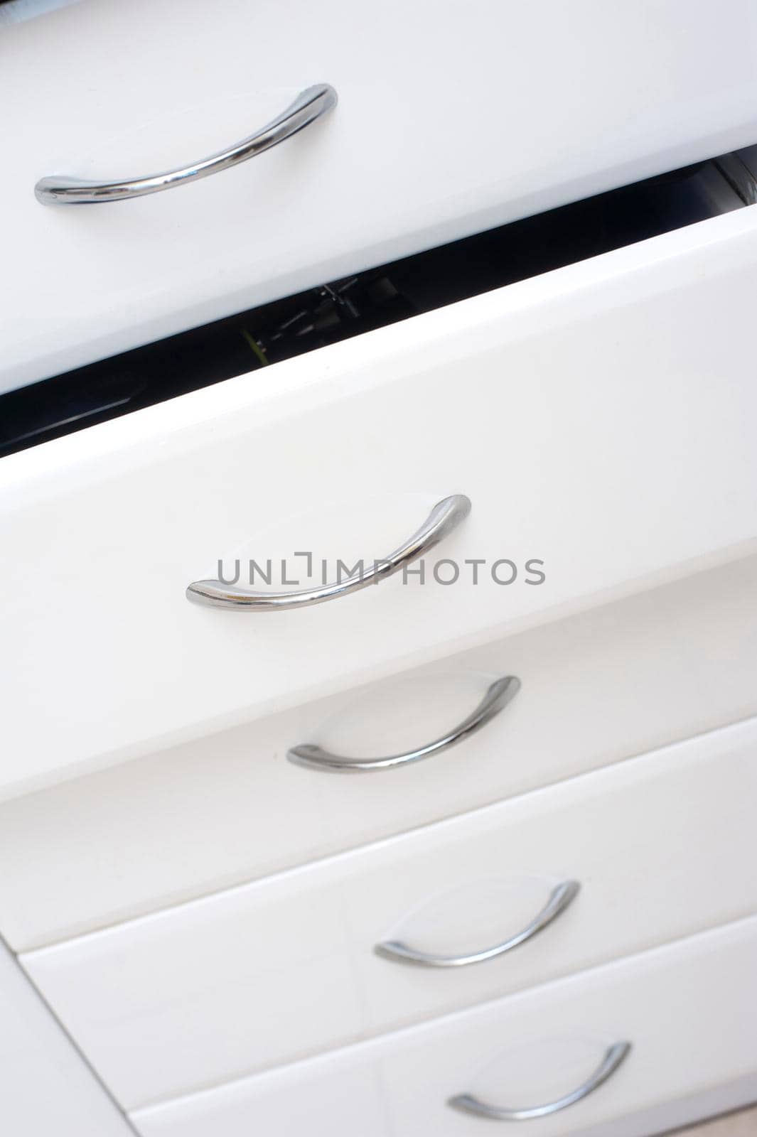 Row of white kitchen drawers with simple metal handles with one slightly open for storage of kitchenware