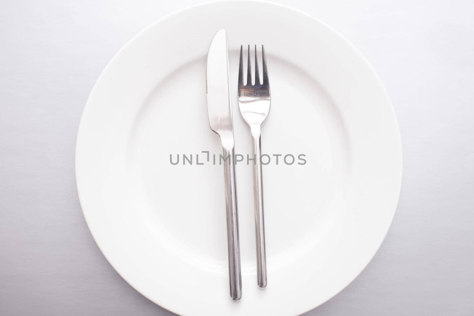 Empty generic white plate with silver knife and fork neatly placed in the centre viewed from overhead