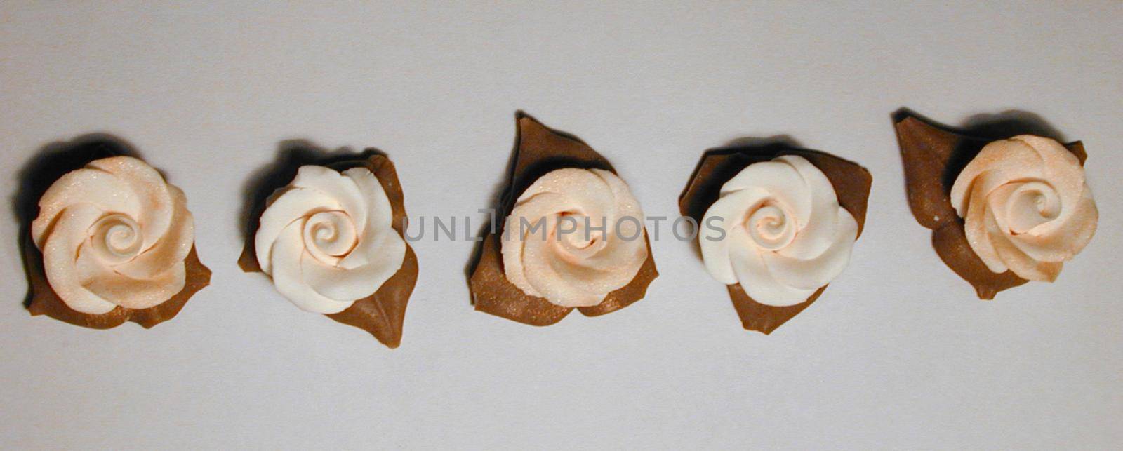 Row of white icing flowers used in baking to decorate a cake viewed from overhead on a grey background in banner format