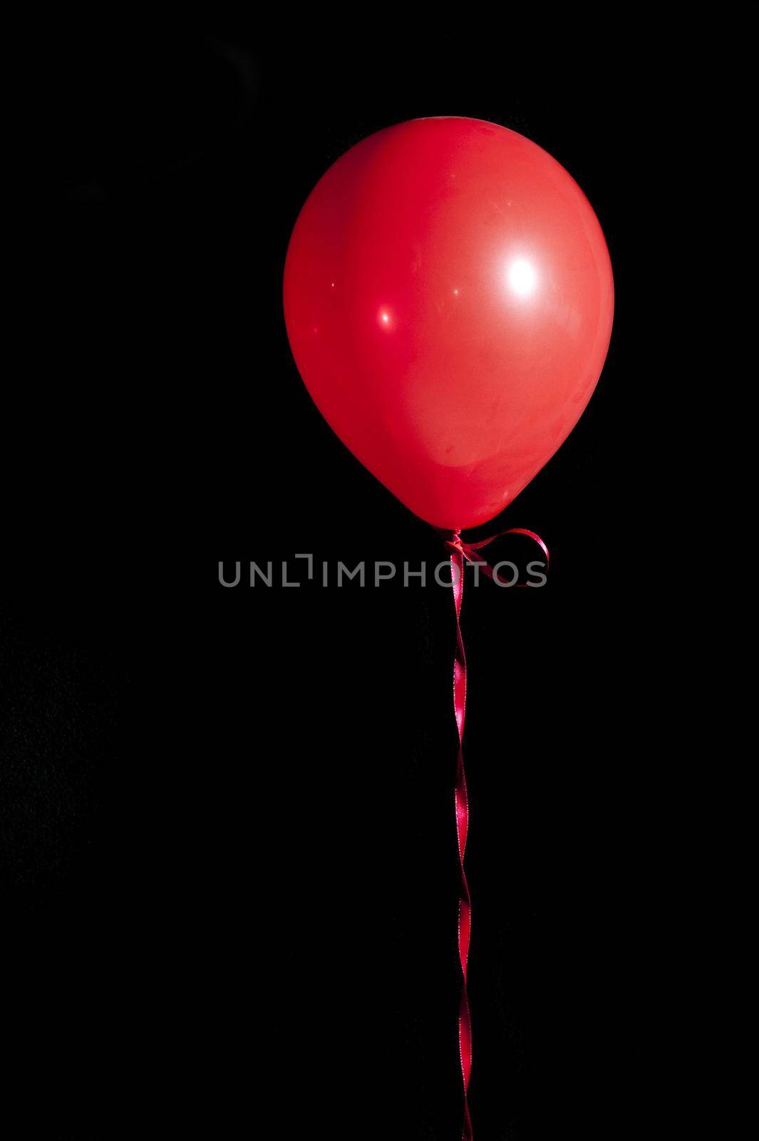 a single red balloon tied with ribbon floating in the air against a black backdrop