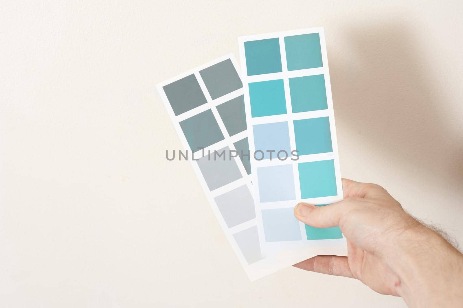 Man holding two cards with sample paint color swatches in grey and blue hues in his hand as he makes a decision on the interior decorating and renovation of his home